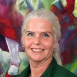 Woman with gray hair smiling in front of vibrant artwork